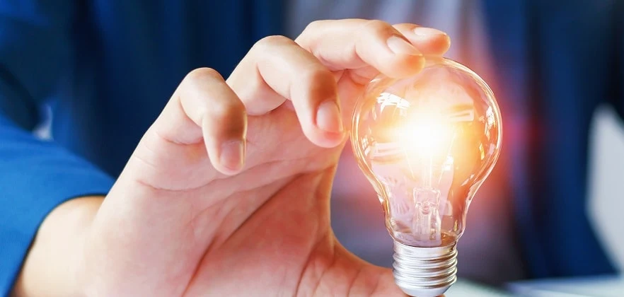 Hand holding an illuminated lightbulb above a laptop and working notes